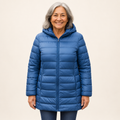 Mature British woman wearing the HELSA Indigo padded jacket on a clean warm off-white studio background